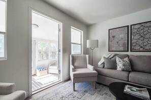 A living room with a sofa, armchair, and coffee table. There are two windows and a door leading to a balcony. - Suniland w/Pool, Hot-tub and sauna! (Fredericksburg)