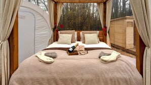Een tentruimte met een bed, champagne, handdoeken en een houten constructie buiten.