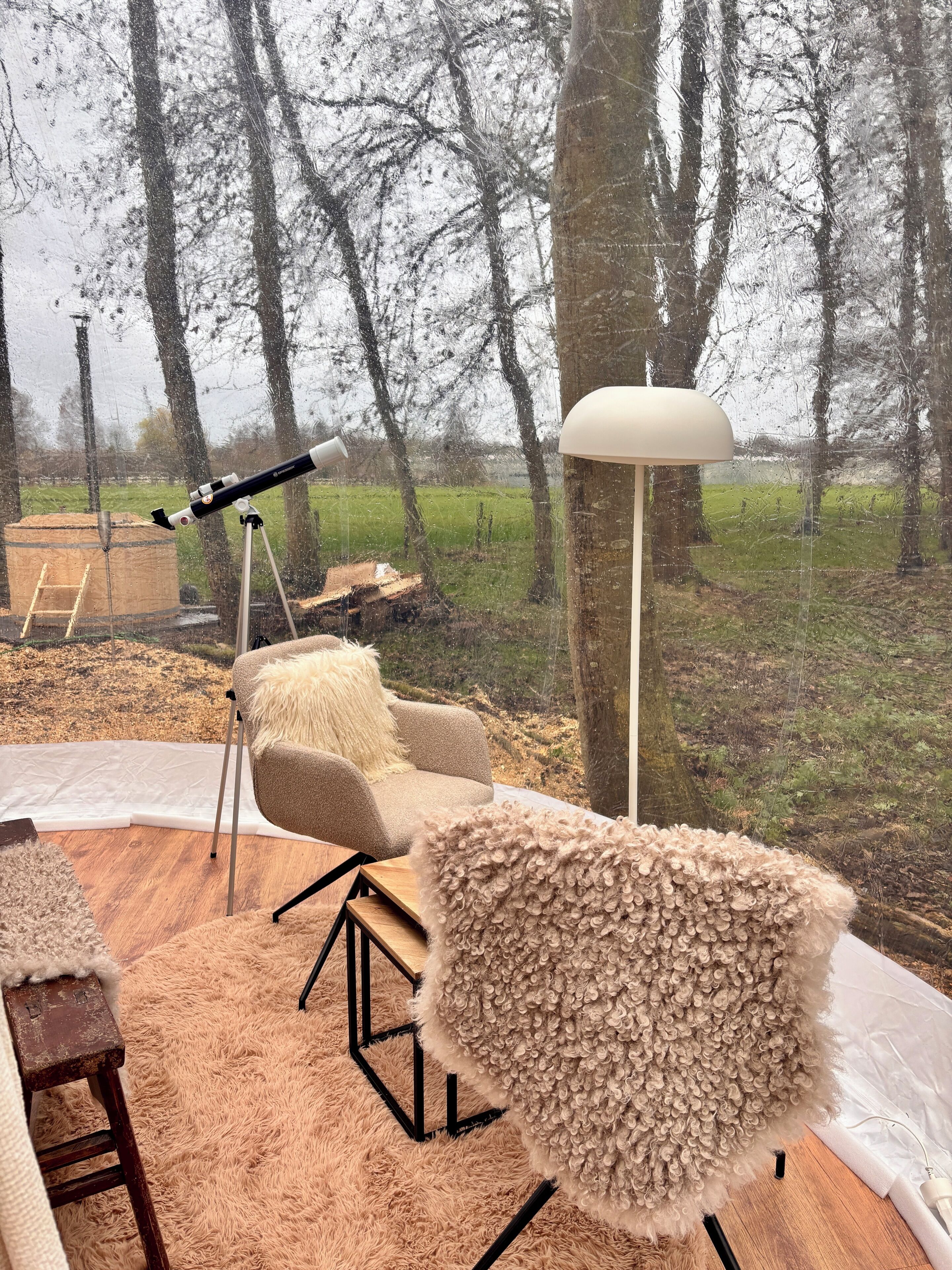 A cozy outdoor seating area with a telescope and a lamp, overlooking a forested landscape.