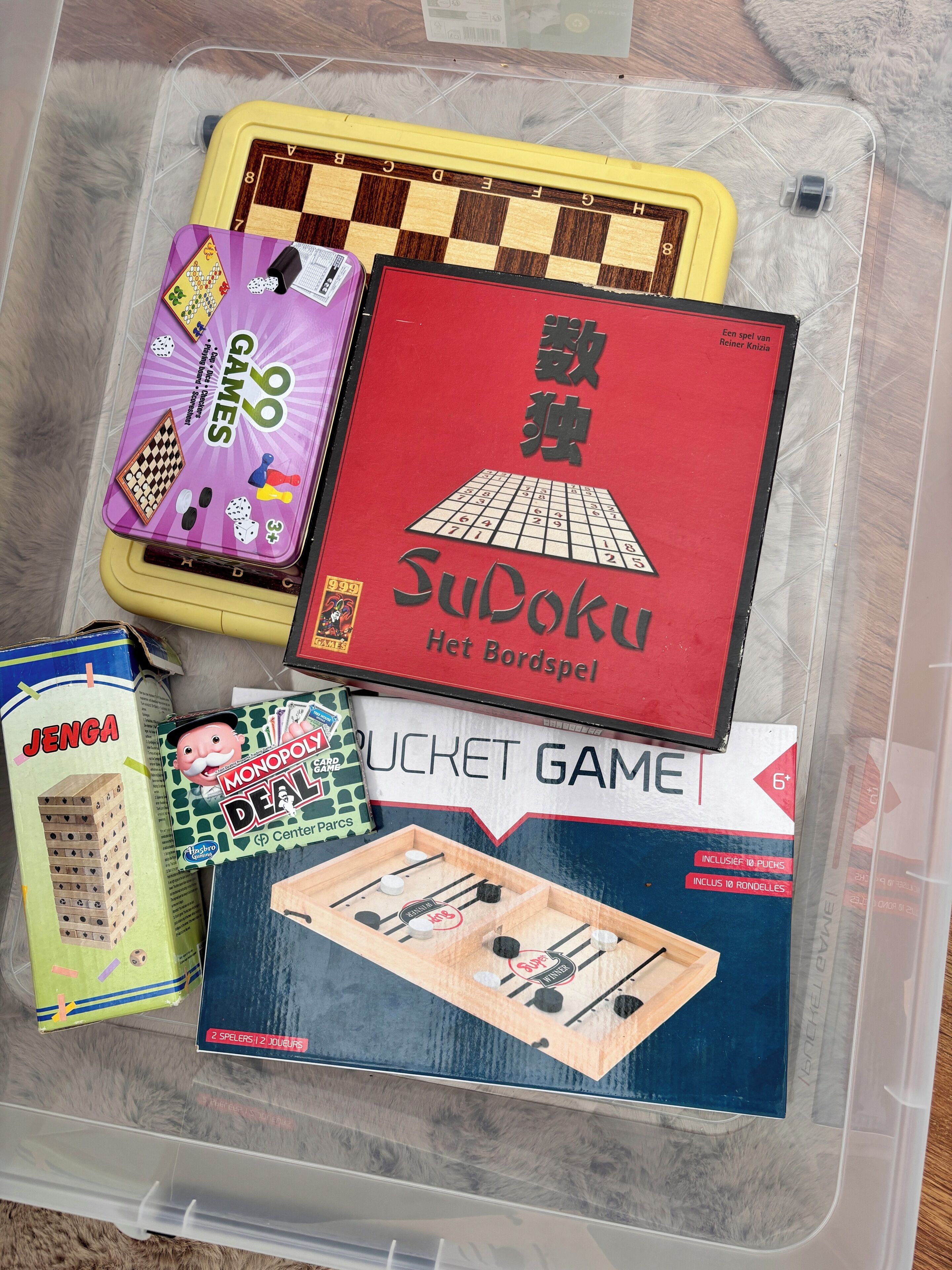Um recipiente de plástico com diversos jogos de tabuleiro, incluindo Jenga, Monopoly, Sudoku e outros.