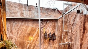 Een badkamer met een douchecabine van glas, marmeren wanden en toiletartikelen aan de muur.