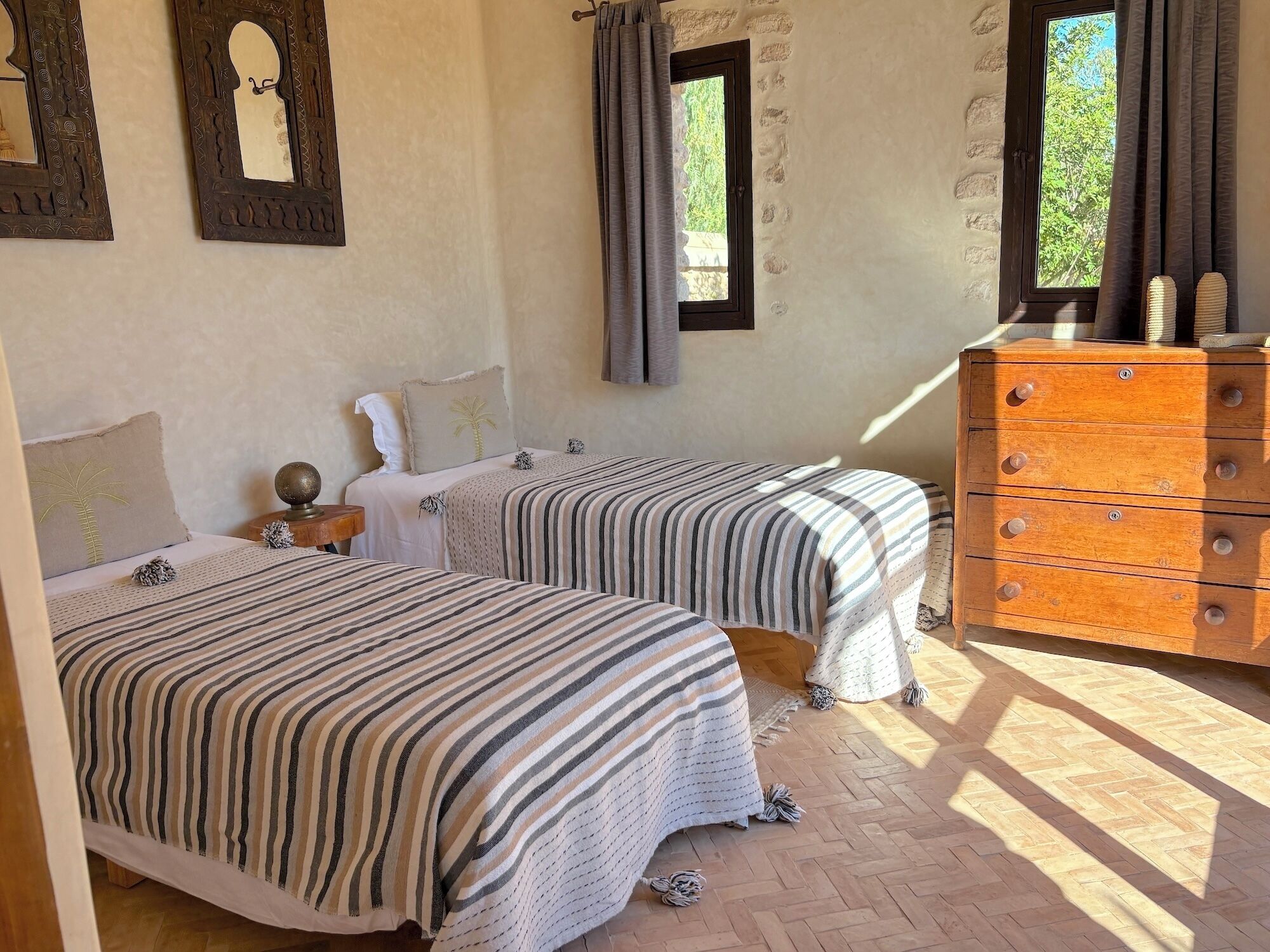 A bedroom with two beds, a wooden dresser, and a window with curtains.