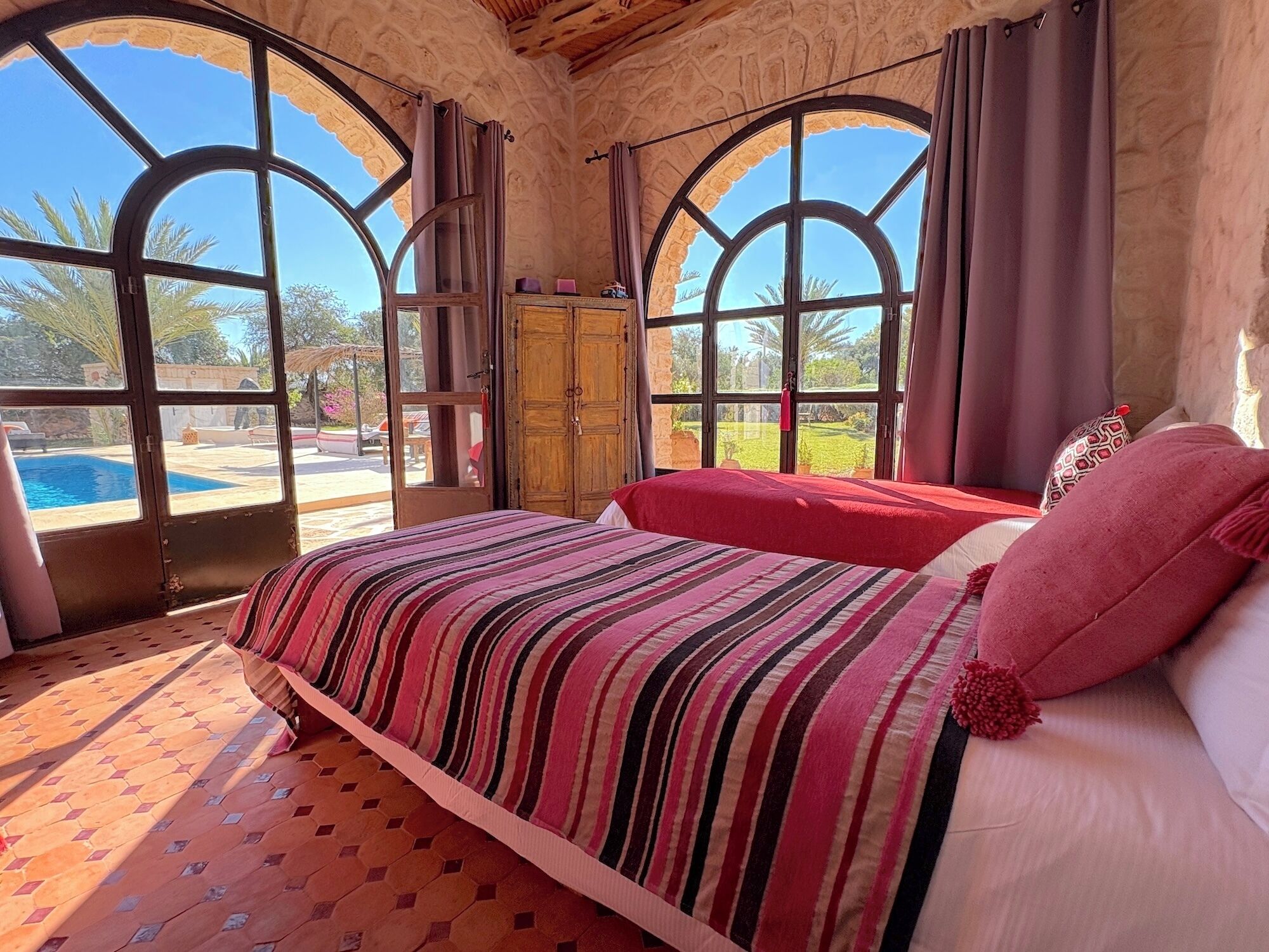 Een slaapkamer met een groot bed, een houten kledingkast en uitzicht op een zwembad door gebogen ramen.
