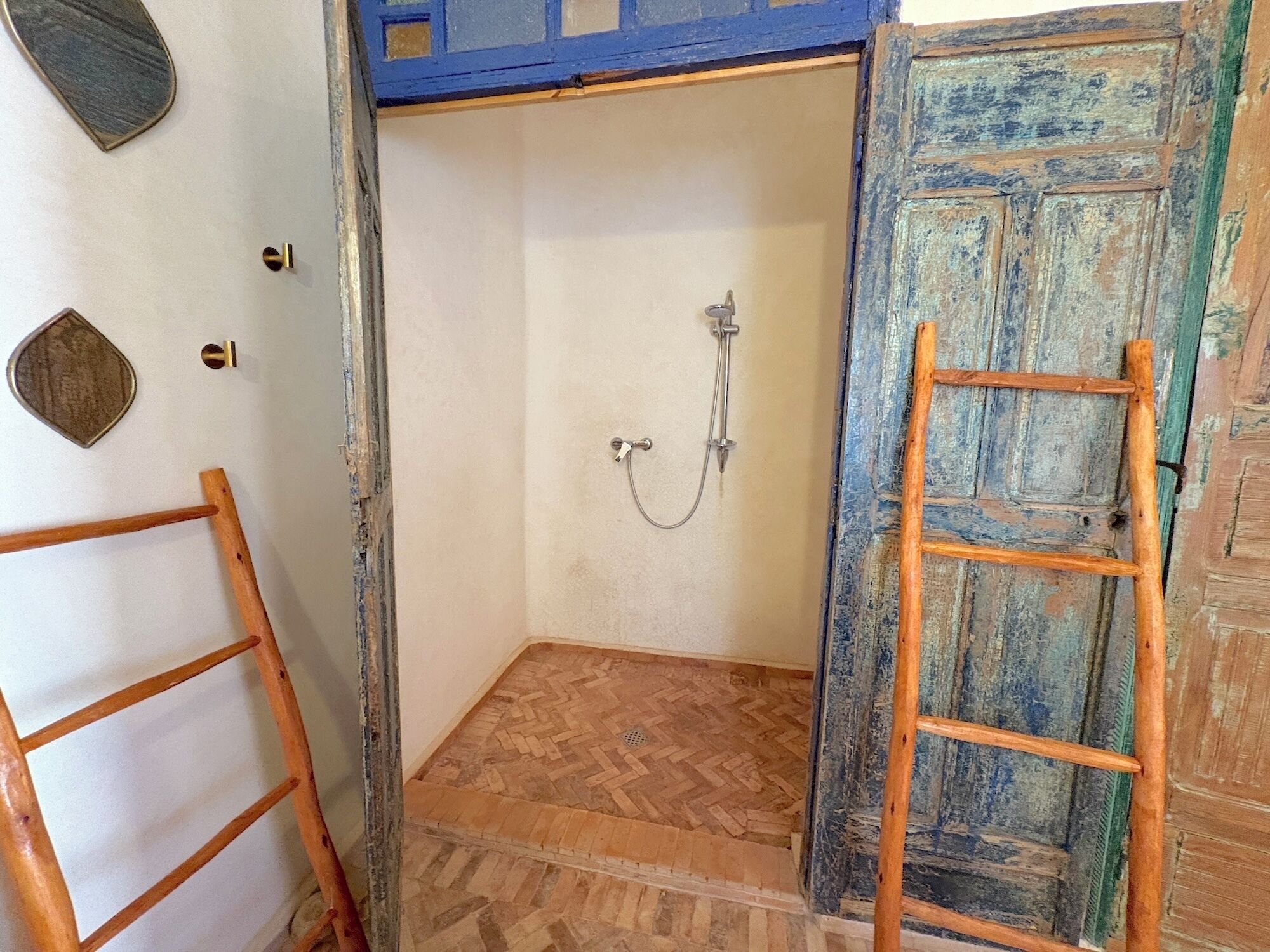 A small, enclosed shower area with a wooden floor, a metal showerhead, and a wooden ladder leaning against the wall.