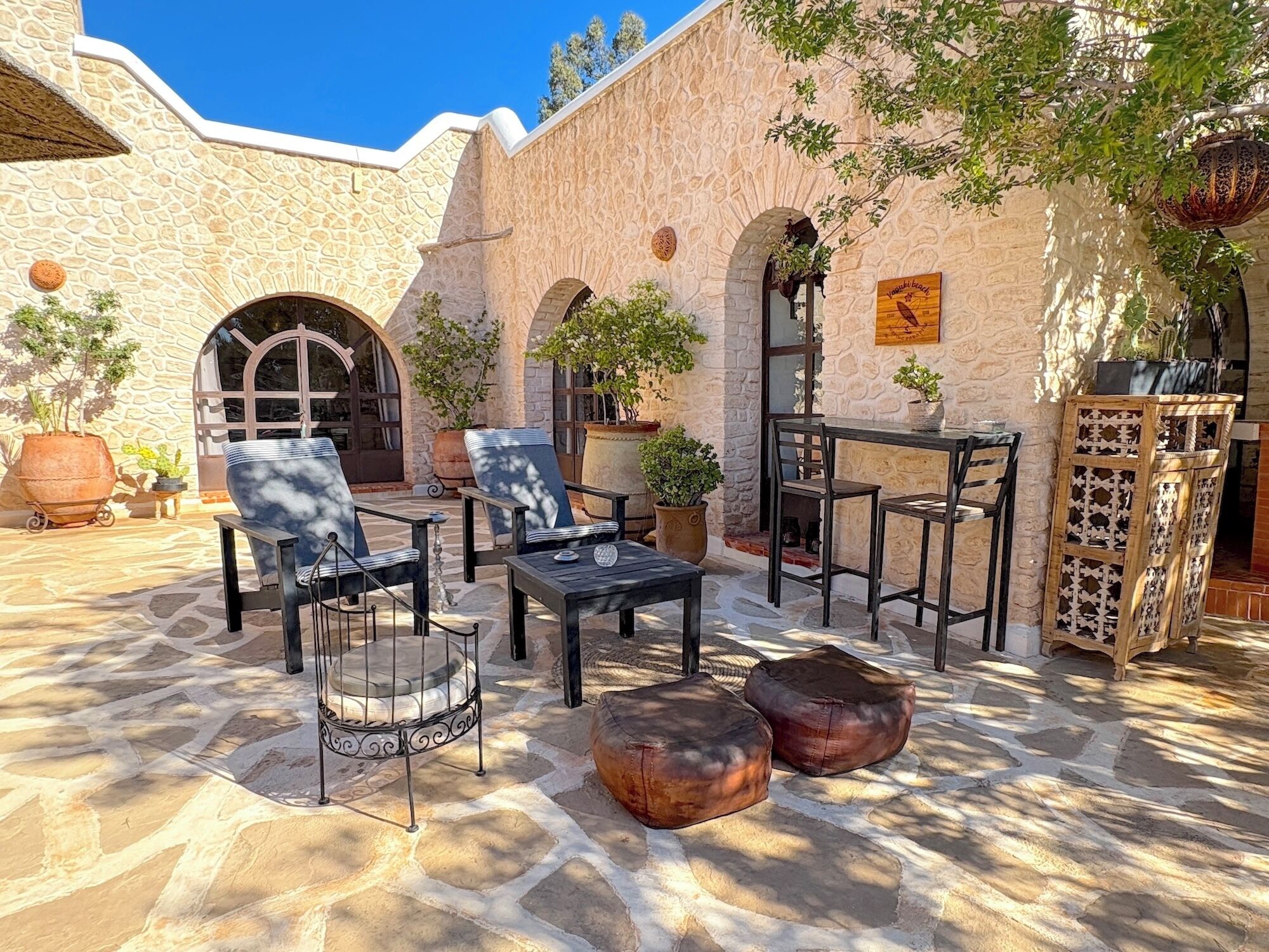 An outdoor patio with stone flooring, seating arrangements, and potted plants.
