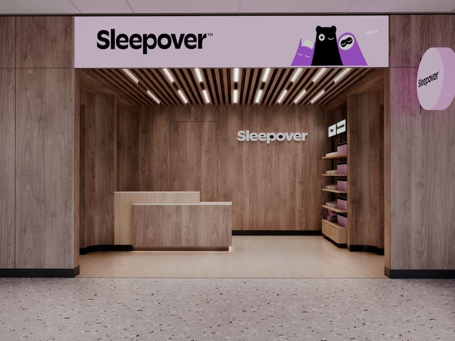 A Sleepover branded store with a wooden interior, a central staircase, and shelves with pink and black items.