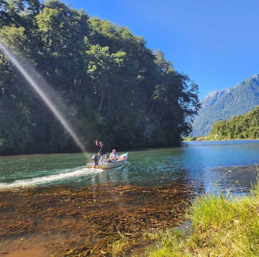 A boat on a calm river with dense forest on one side and mountains in the background.