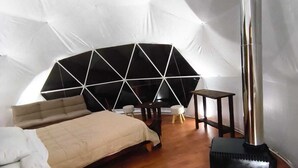 A tented room with a bed, a table, and a portable heater. - Domo Valle El Encanto Peulla (Puerto Varas)