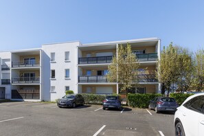 Ein mehrstöckiges Wohngebäude mit Balkonen, einem Parkplatz und blauem Himmel.