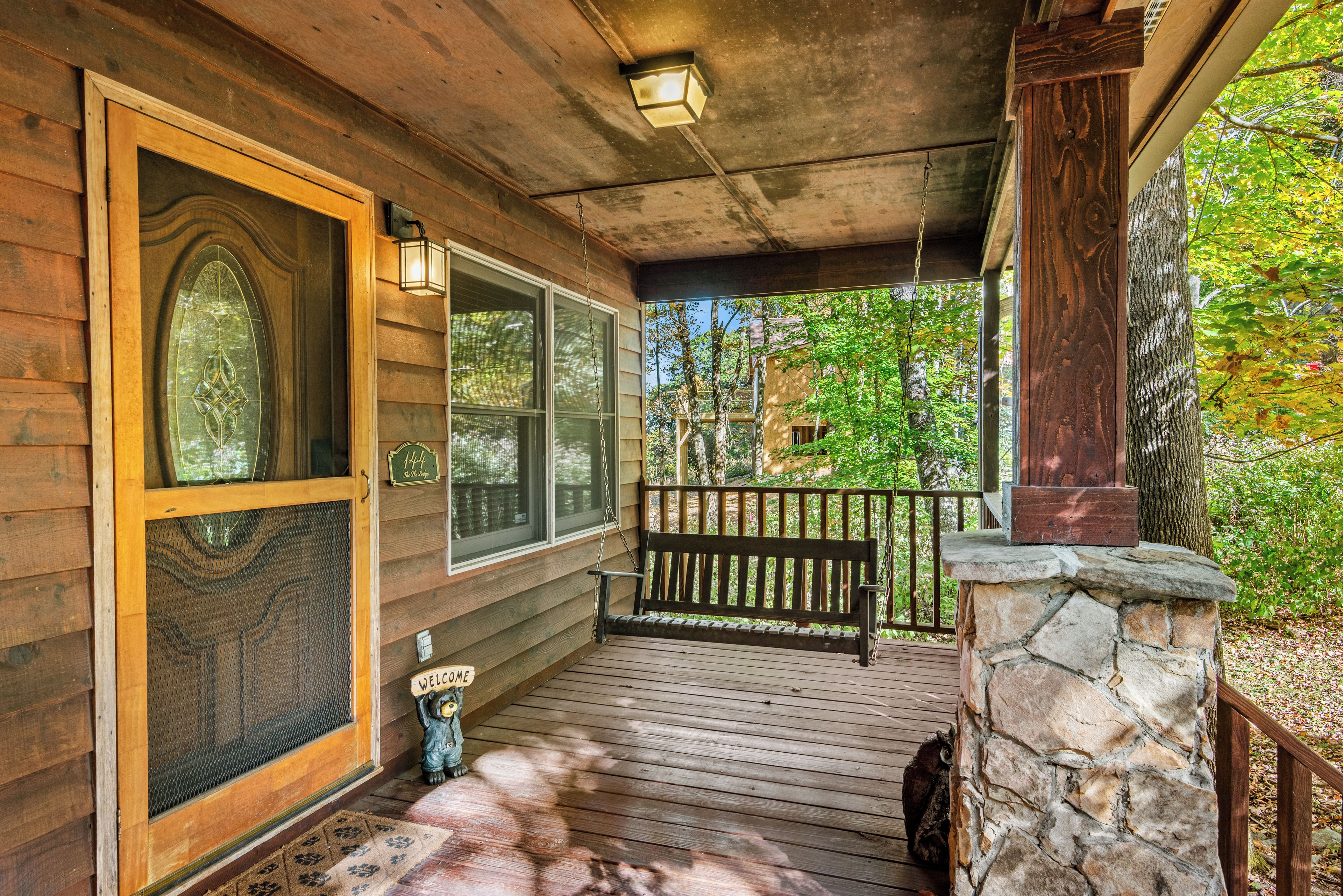 A wooden porch with a stone wall, a bench, and a welcome sign.