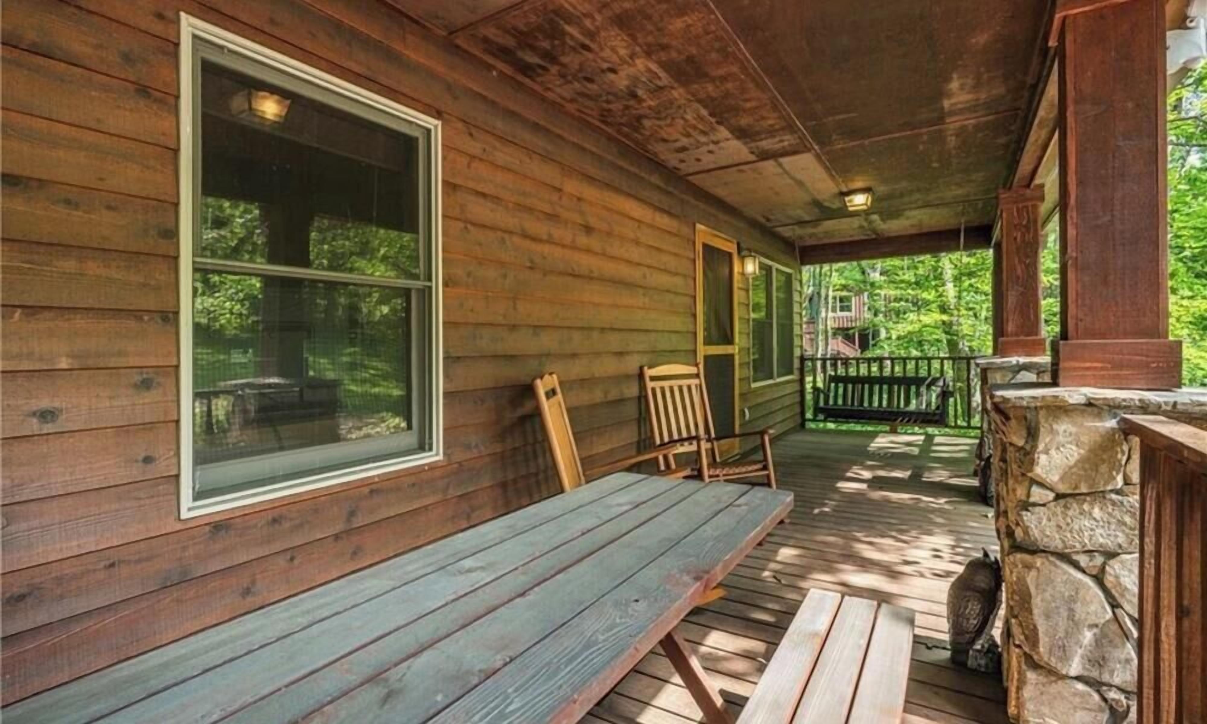 A wooden cabin with a porch, a bench, and a stone wall.
