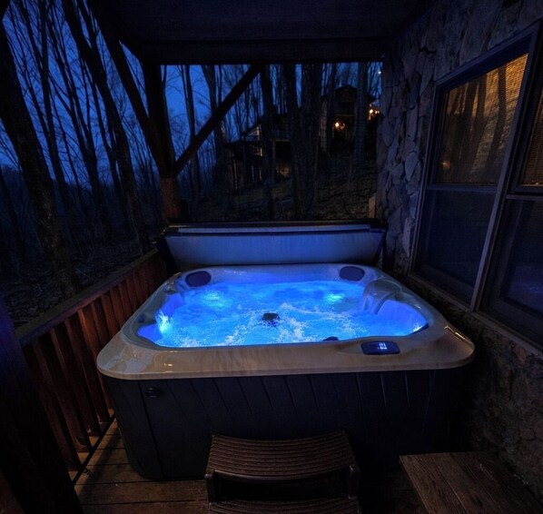 Un bain à remous doté d’une terrasse en bois et de murs en pierre, entouré d’arbres.