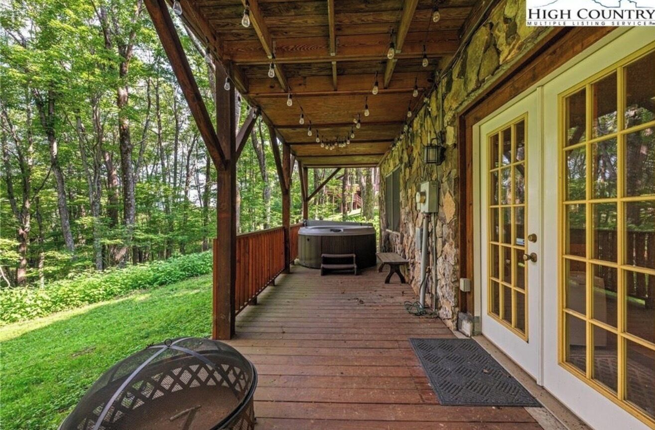 A covered porch with a hot tub, wooden deck, and a stone wall.
