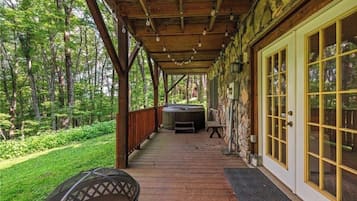 A covered porch with a hot tub, wooden deck, and a stone wall.