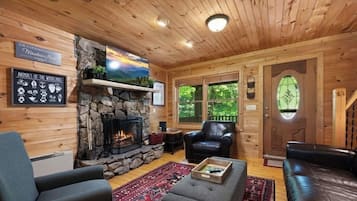 A cozy log cabin interior with a stone fireplace, leather furniture, and a sign reading "Animals of the Woodland Hills".