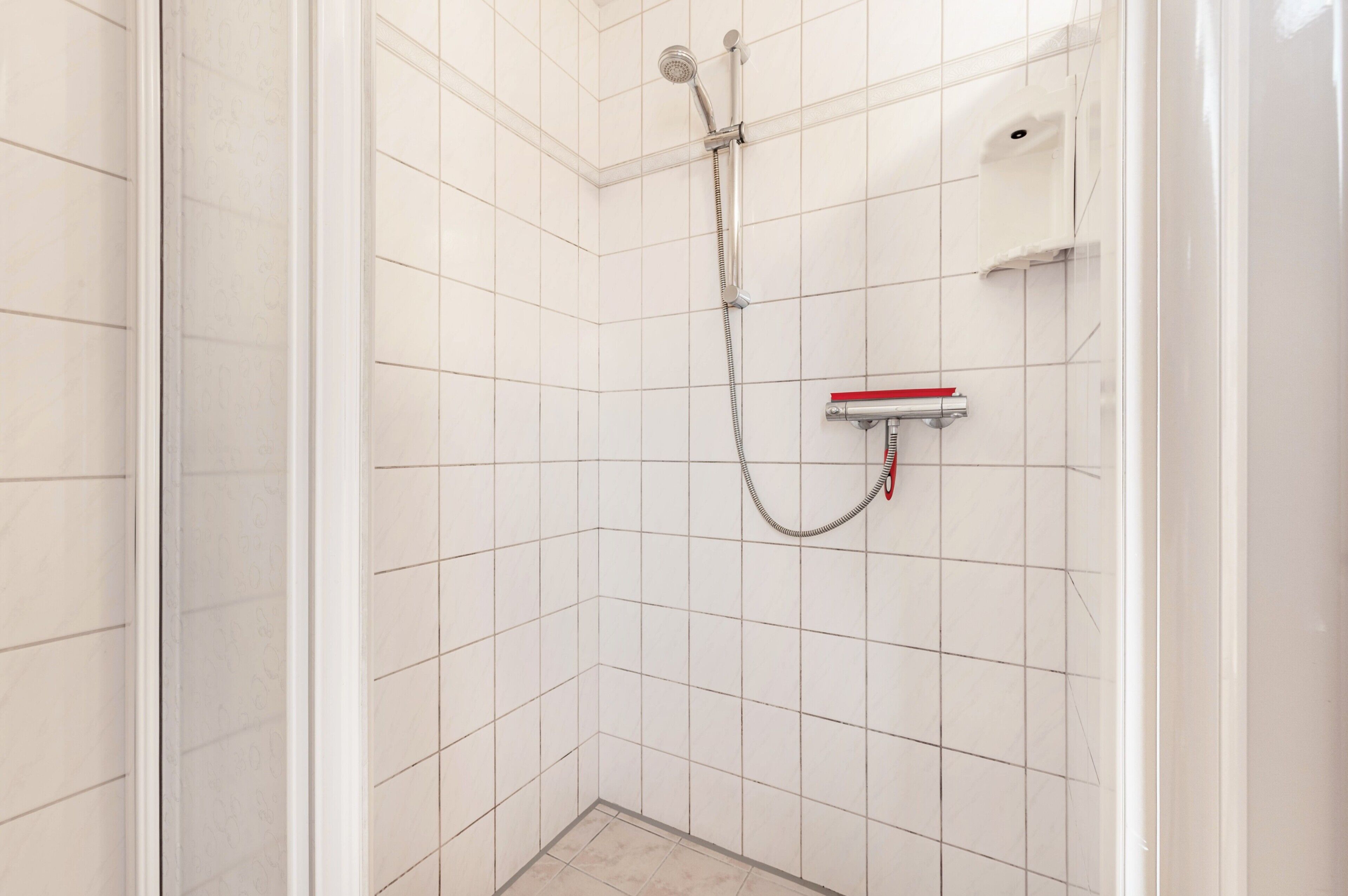 A shower with a handheld showerhead, a handheld shower attachment, and a soap dispenser on the wall.
