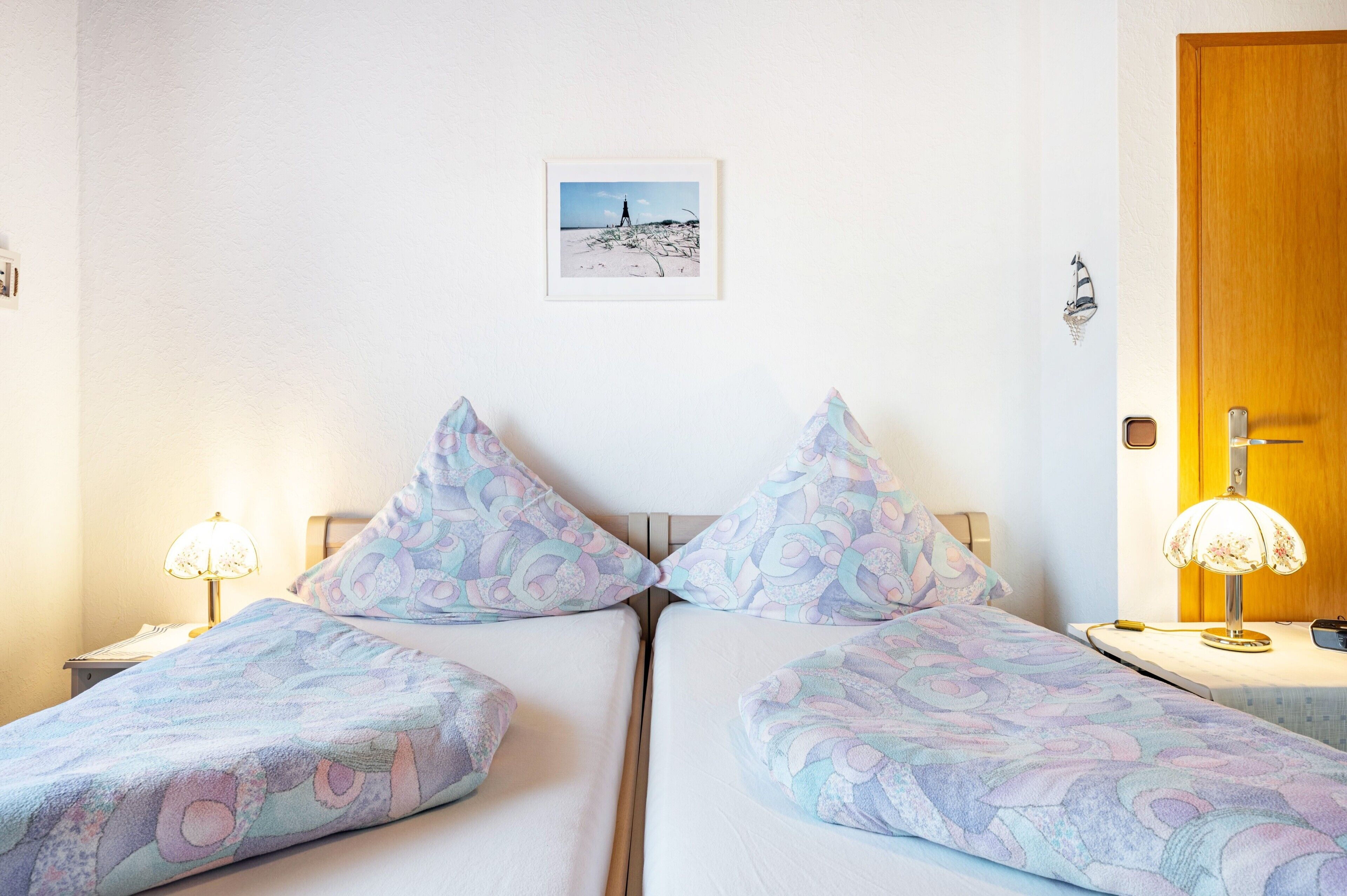 Un lit double avec une literie à motifs, une table de chevet avec une lampe, un tableau encadré au mur et une porte en bois.