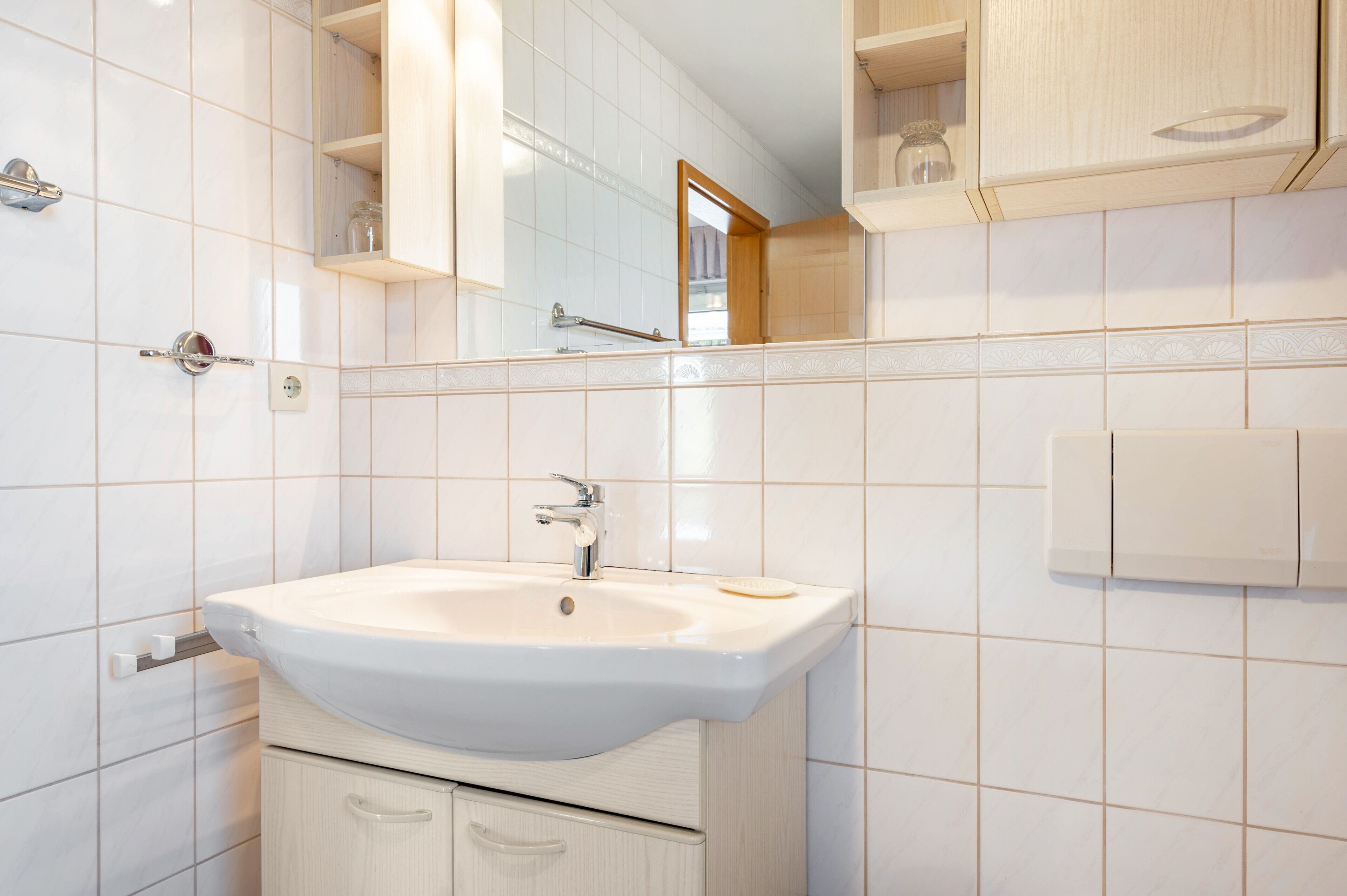 A bathroom with a white sink, mirror, and tiled walls.