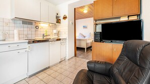 Una cocina compacta con armarios blancos, una cafetera y un televisor sobre un mueble de madera.