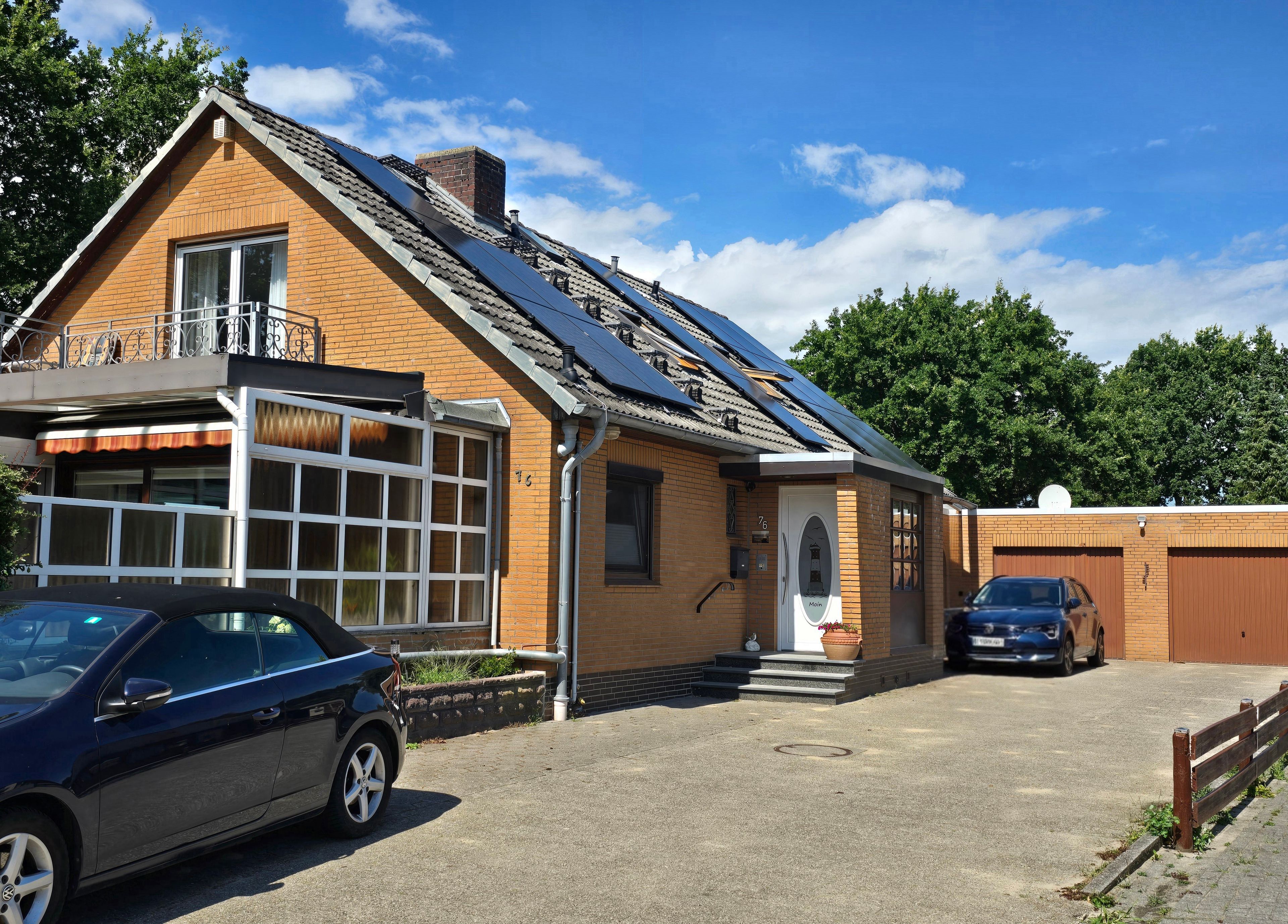 Ein zweistöckiges Gebäude mit geneigtem Dach und Solaranlage, mit einem Auto auf der Auffahrt.