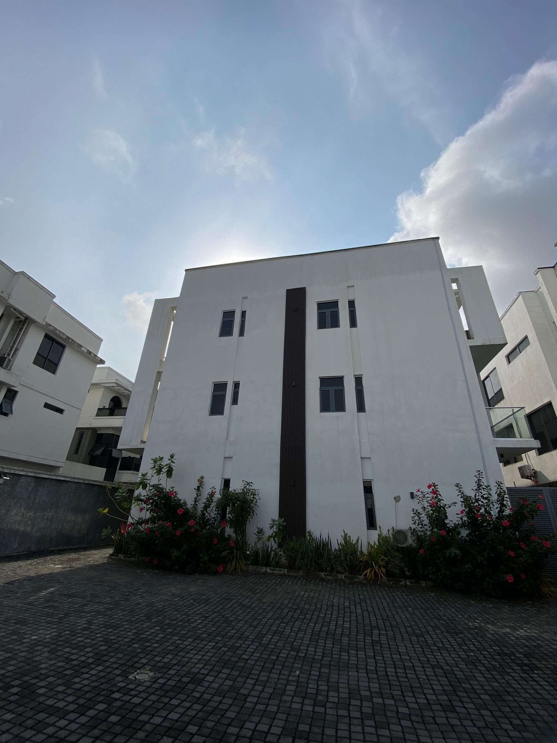 A modern building with a central vertical feature, surrounded by a paved area with plants.