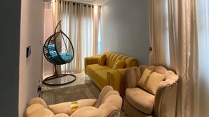 A modern living room with a yellow sofa, beige armchairs, a hanging chair, and a patterned rug. - ETD SUPPORT (Lekki)