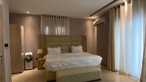 A modern bedroom with a large bed, bedside tables, a fan, and a window with curtains. - ETD SUPPORT (Lekki)