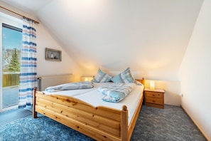 Un dormitorio con una cama de madera, una mesita de noche, una lámpara, un cuadro enmarcado y vistas al exterior.