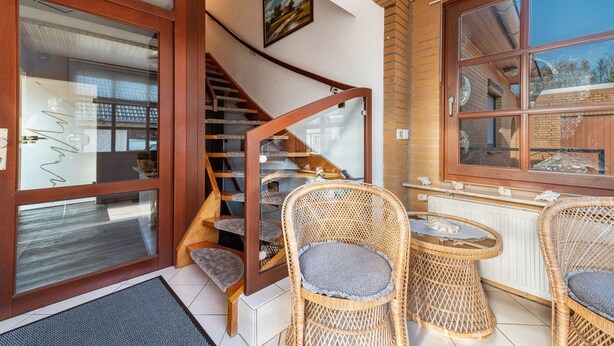 Een trap die leidt naar een tweede verdieping, met rieten stoelen, een kleine tafel en een raam met uitzicht.