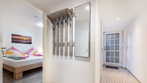 A bedroom with a bed, a wall-mounted mirror, and a door leading to another room. - Apartment "Souterrain" with Private Terrace, Garden, and Wi-Fi (Cuxhaven)