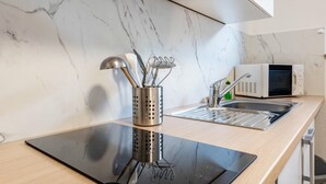 A modern kitchen with a marble backsplash, a stainless steel utensil holder, a microwave, and a sink with a faucet. - Apartment "Souterrain" with Private Terrace, Garden, and Wi-Fi (Cuxhaven)