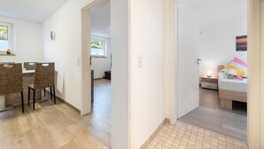 A modern apartment with a dining area, a bedroom with a bed and nightstand, and a bathroom with a sink and window. - Apartment "Souterrain" with Private Terrace, Garden, and Wi-Fi (Cuxhaven)