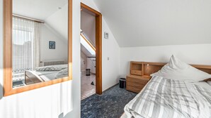 Une chambre à coucher avec un lit, une table de chevet en bois, une commode, un miroir et une vue sur la salle de bain.