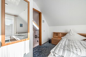 A bedroom with a bed, a wooden nightstand, a dresser, a mirror, and a view of a bathroom. - Room 'Südzimmer' with Private Terrace, Garden Access and Wi-Fi (Cuxhaven)