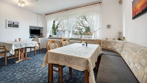 Une pièce comprenant une table à manger, des chaises, un canapé, un téléviseur et une fenêtre avec des rideaux.