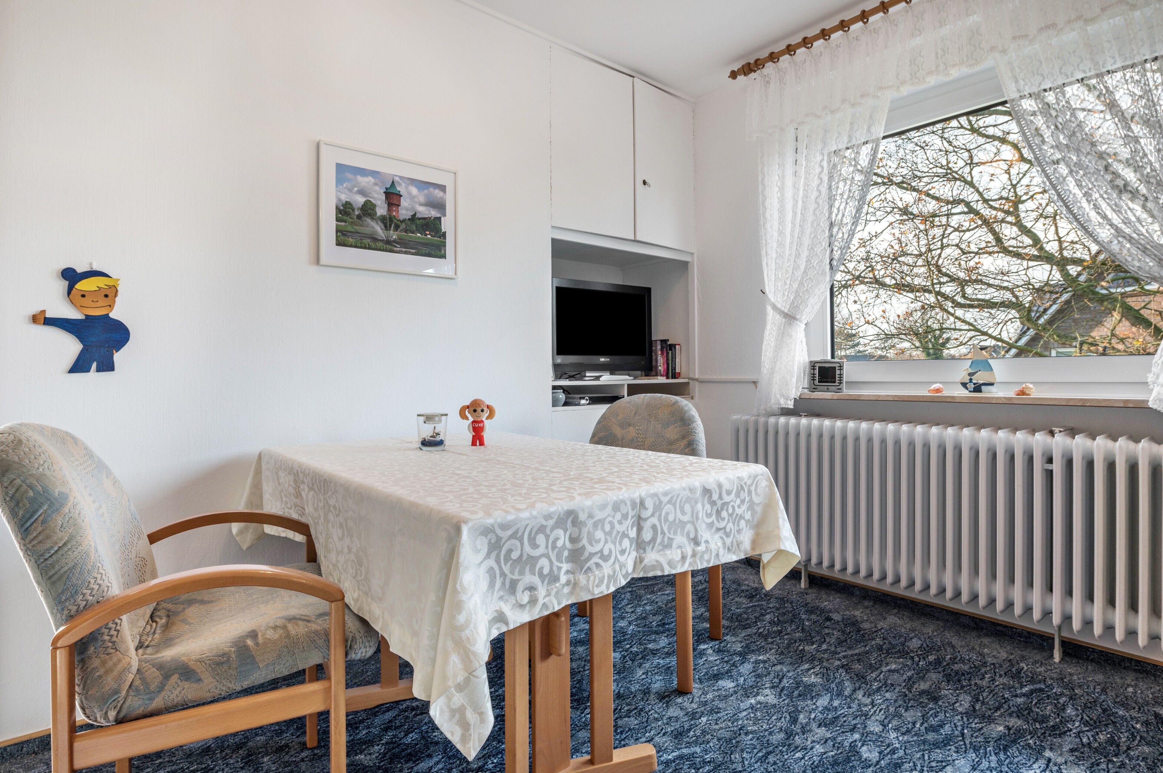 A room with a dining table, chairs, a radiator, a TV, and a window with a view.