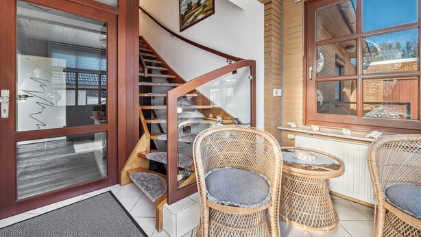 Un escalier avec une rampe en bois menant à un palier où se trouvent des chaises en osier et une table.