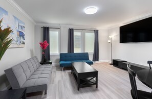 Un salon moderne avec un canapé gris, un canapé bleu, une table basse noire et un téléviseur fixé au mur.