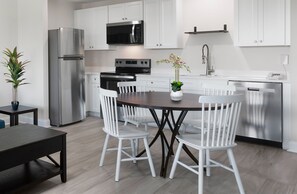 Une cuisine moderne avec des meubles blancs, des appareils en acier inoxydable, une table à manger avec des chaises blanches et une plante en pot.