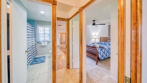 Un passadís que condueix a una habitació amb un llit, un ventilador de sostre i un bany amb dutxa i una barra de tovalloles.