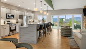 A modern kitchen with a central island, bar stools, and a view of a mountainous landscape through large windows. - Villa w/ Mountain views, golf, hot tub - 20 min from Asheville. Pet friendly! (Fletcher)