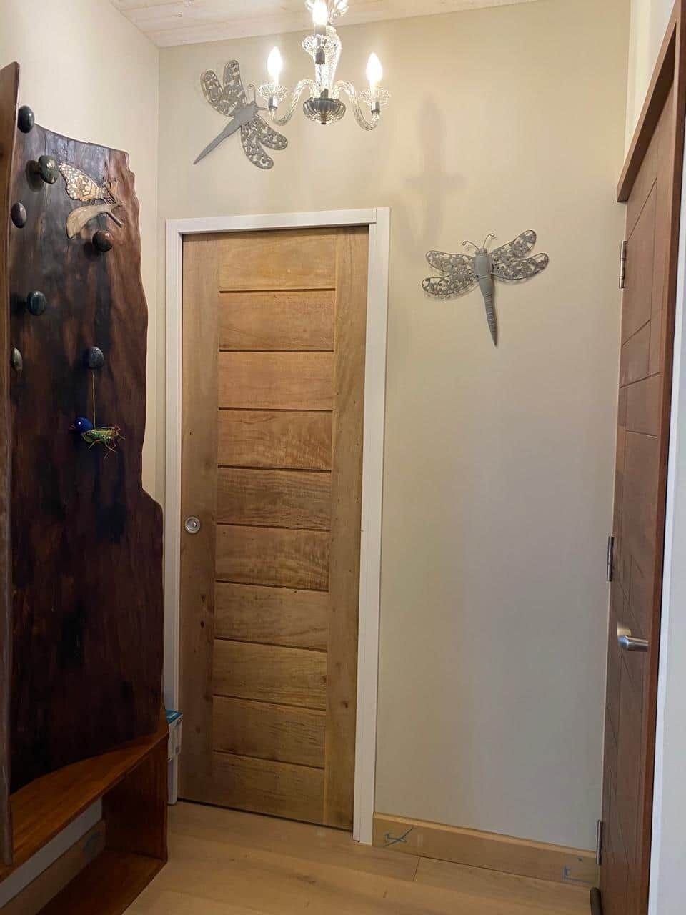 Una puerta de madera con diseño de paneles, un candelabro y decoraciones de mariposas en la pared.
