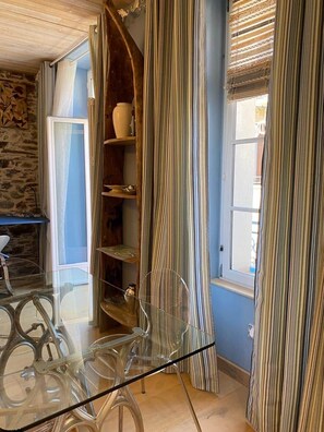 A room with a glass table, striped curtains, a stone wall, and a window with blinds. - Jasmine, pretty hat. The breath of fresh air. (Bagnères-de-Luchon)