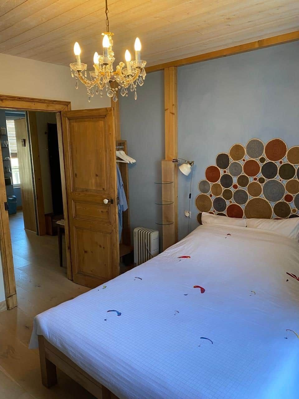 Een slaapkamer met een houten plafond, een kroonluchter, een bed met een gestreept hoofdeinde en een nachtkastje.