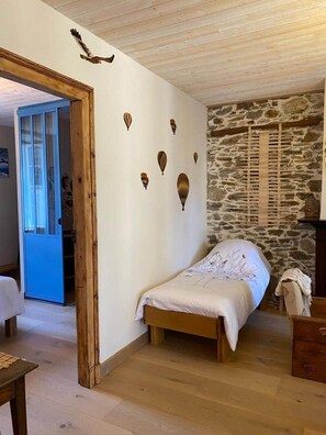 A bedroom with a stone wall, a wooden bed, and a blue door. - Jasmine, pretty hat. The breath of fresh air. (Bagnères-de-Luchon)
