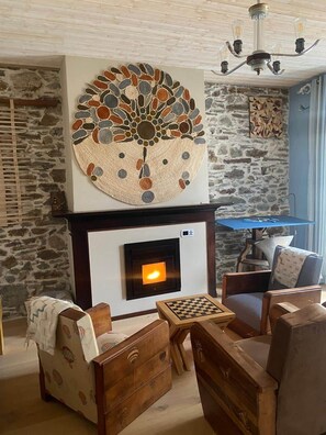 A cozy living room with a stone wall, a fireplace, a chess table, and wooden furniture. - Jasmine, pretty hat. The breath of fresh air. (Bagnères-de-Luchon)