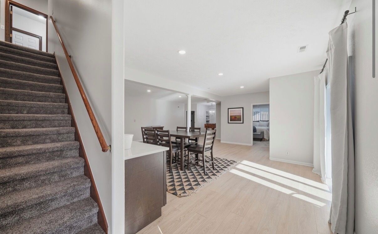A modern interior with a staircase, a dining area with a table and chairs, and a kitchen area.