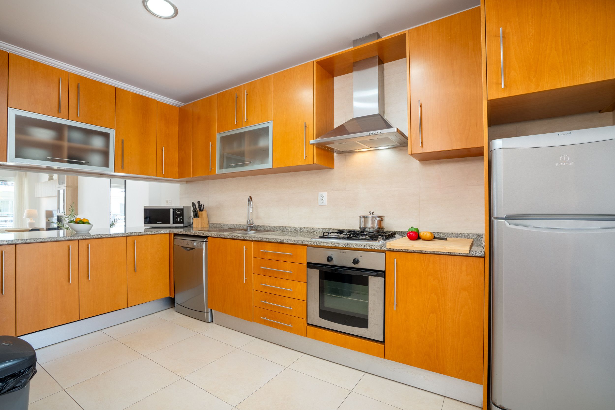 A modern kitchen with wooden cabinets, stainless steel appliances, and a tiled floor.