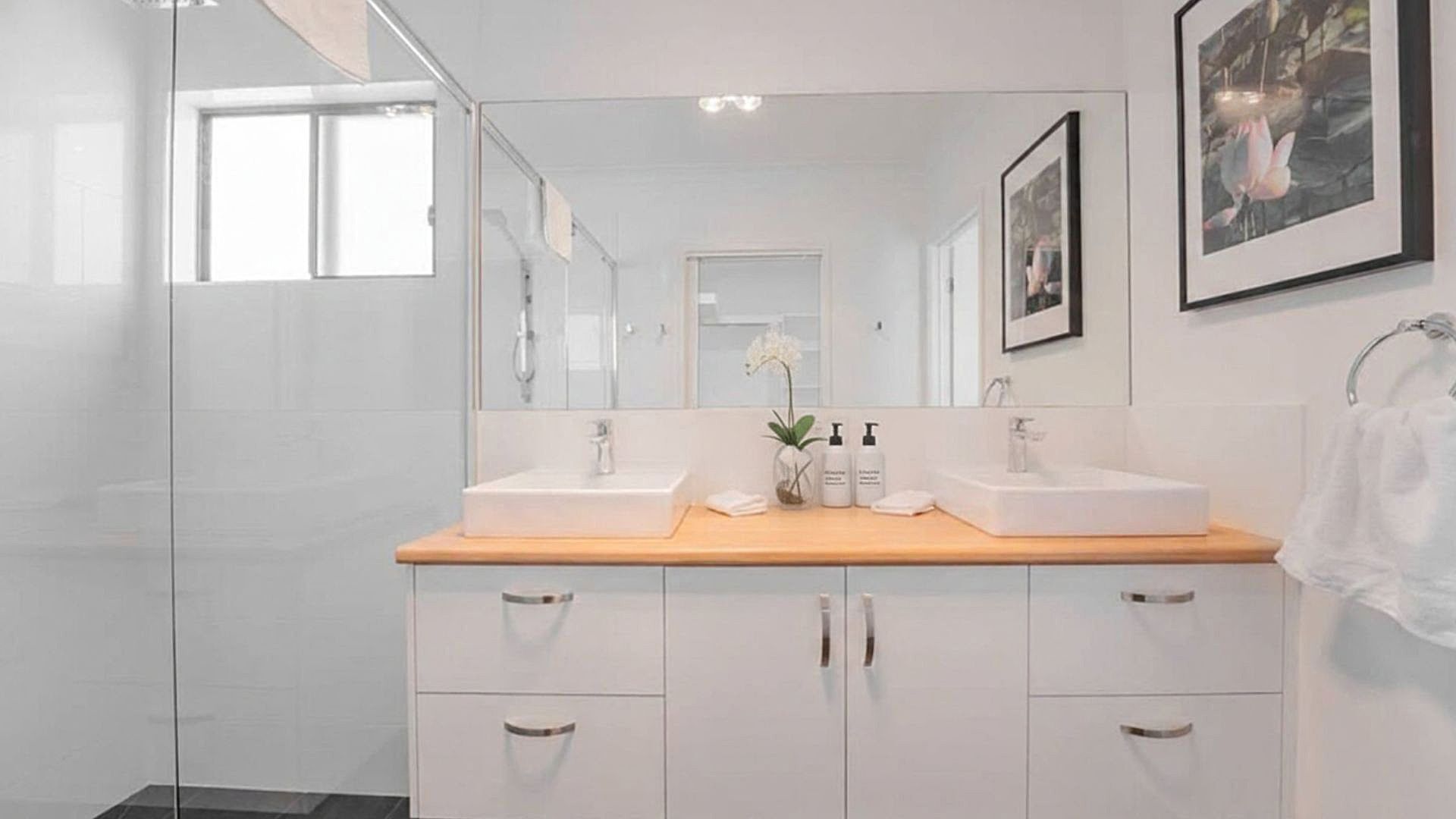 Een moderne badkamer met twee wastafels, een grote spiegel en een houten aanrecht.