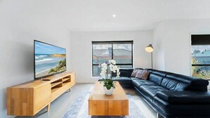 Ein modernes Wohnzimmer mit großem Flachbildfernseher, einer schwarzen Ledersofa, einem Holztisch und einer Topfpflanze.
